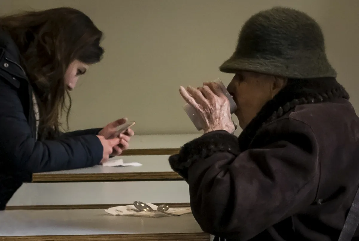 Young woman focused on her phone across a table from an older woman drinking